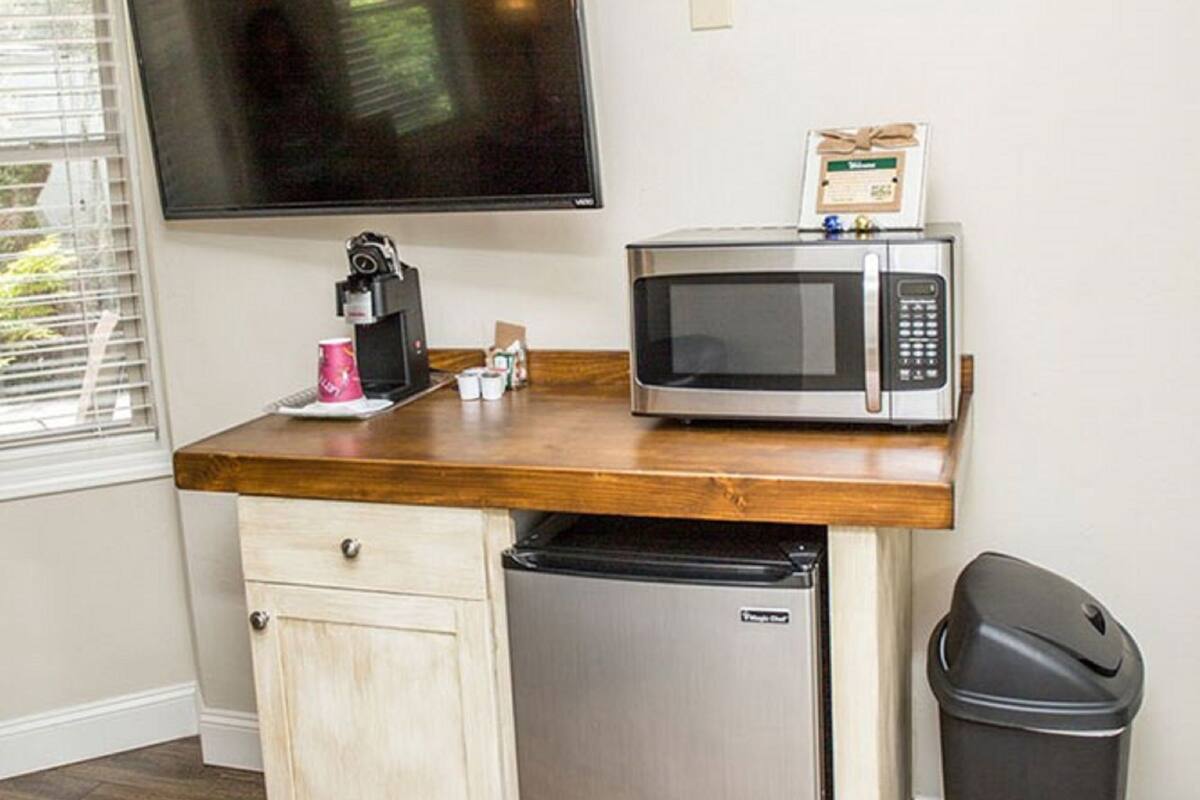 A compact kitchenette with a microwave, a small refrigerator, a trash bin, and a flat-screen TV mounted on the wall.