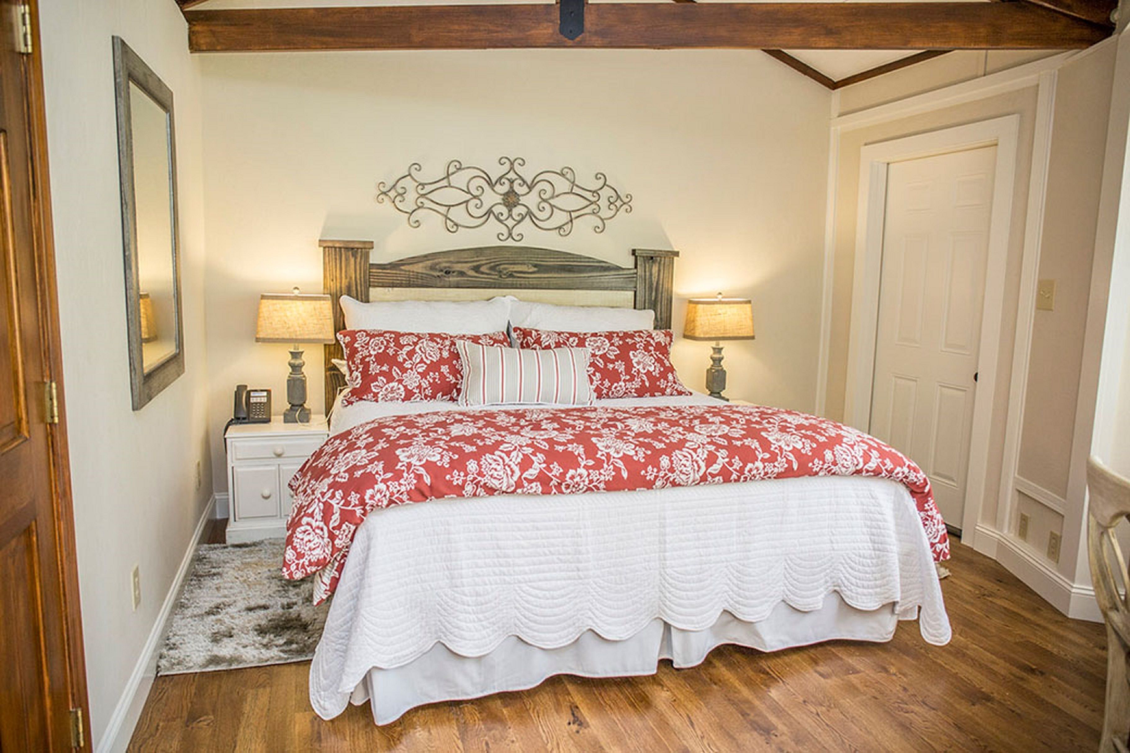 Een slaapkamer met een houten bed, witte beddengoed, een decoratief hoofdeinde, bedlampjes en een houten vloer.