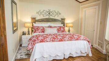 A bedroom with a wooden bed, white bedding, a decorative headboard, bedside lamps, and a wooden floor.