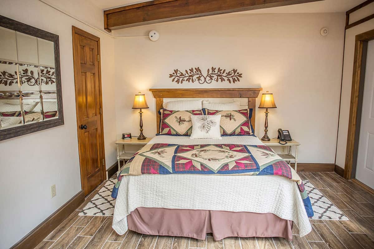 A bedroom with a bed, two bedside lamps, a decorative headboard, a mirror, and a patterned rug.