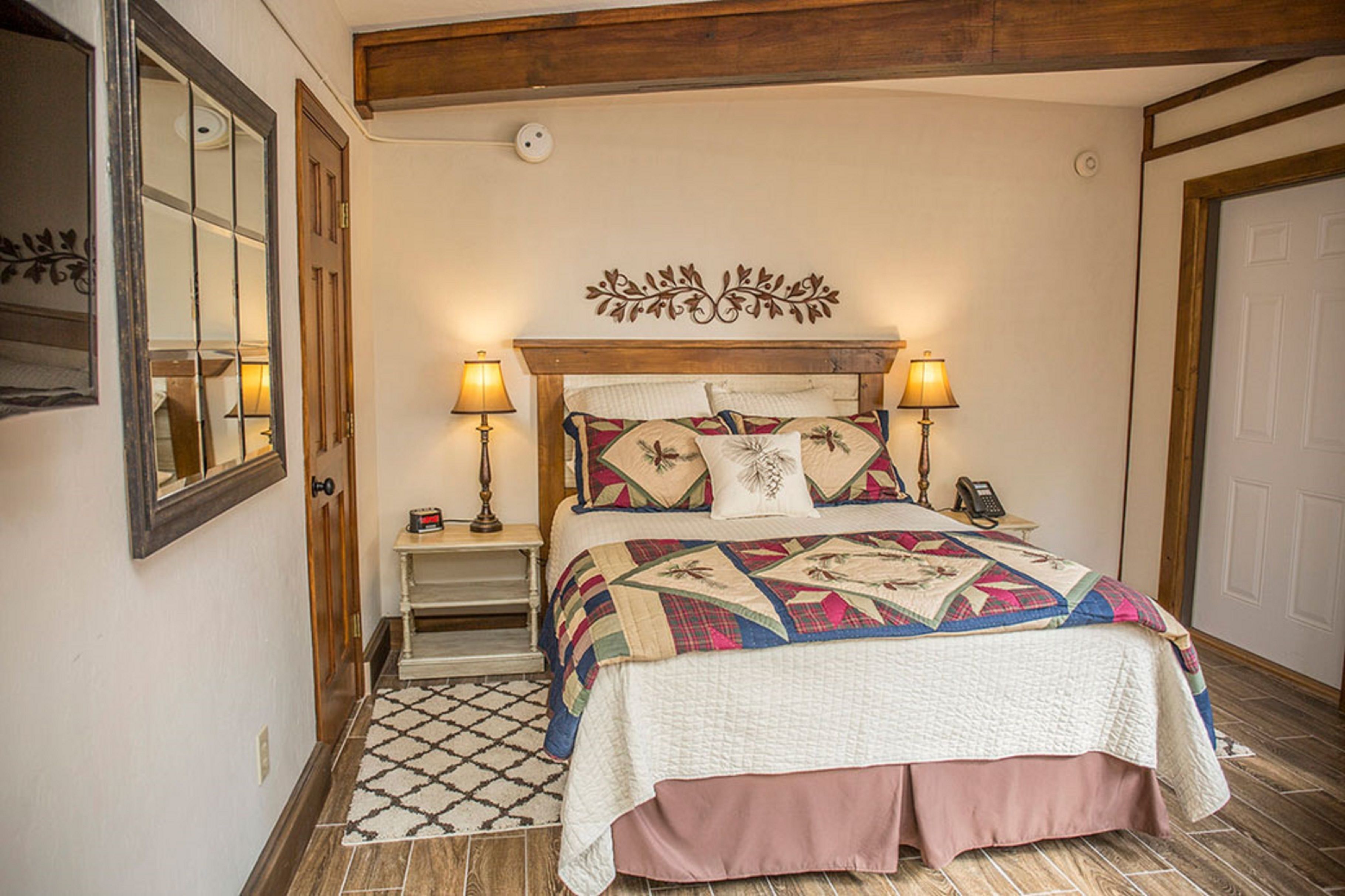 Quarto com cama, duas luminárias de apoio, mesa de cabeceira, espelho e tapete estampado.