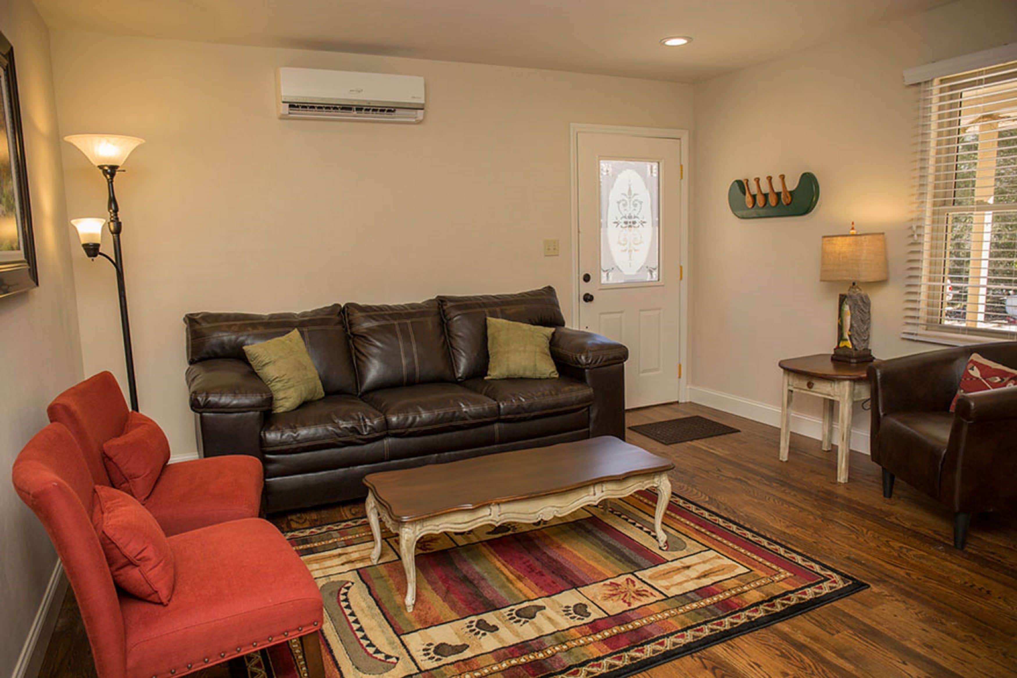 A living room with a brown leather couch, a red armchair, a wooden coffee table, and a patterned rug.