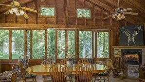 A rustic wooden dining area with a large table and chairs, large windows with a forest view, and a fireplace. - Brook Trout Inn (Sapphire)