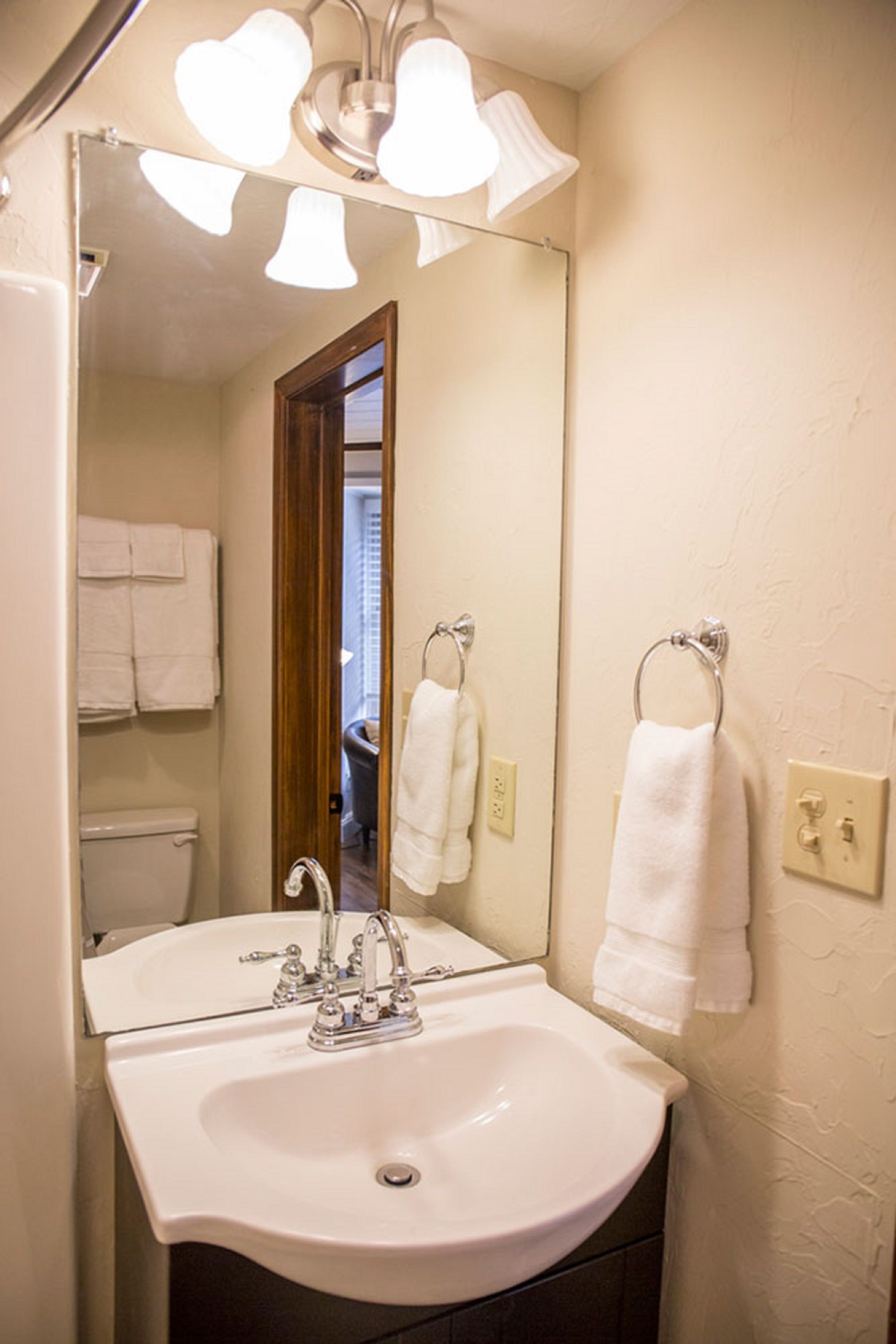 A bathroom with a white sink, a mirror, and two towels hanging on towel rings.