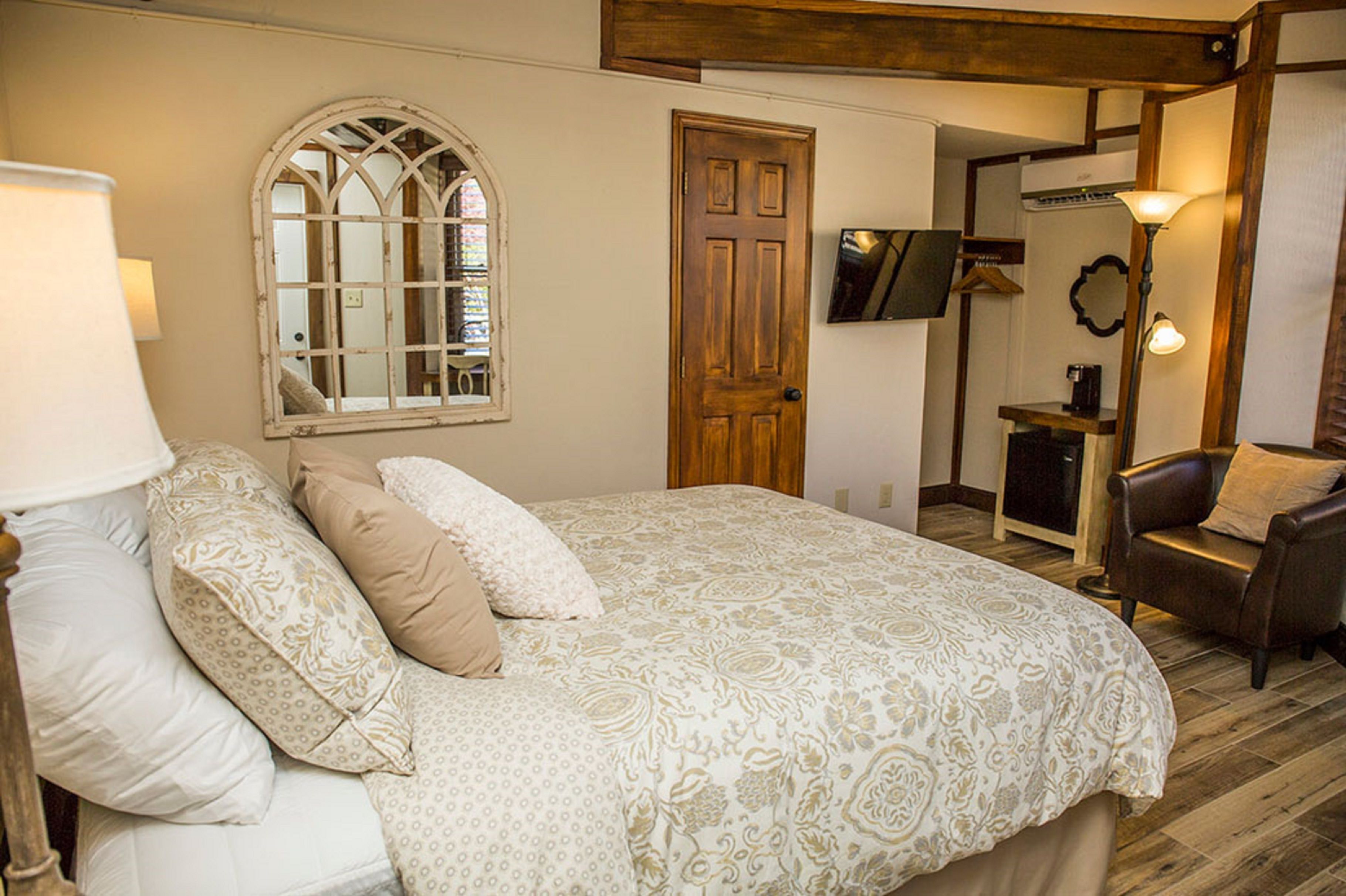 A bedroom with a large bed, a wooden door, a TV mounted on the wall, and a chair.