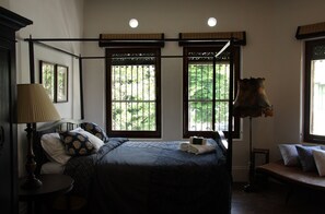 A bedroom with a four-poster bed, a bedside table with a lamp, and a bench with pillows. - The Bhuthorn Bed and Breakfast (Bangkok)