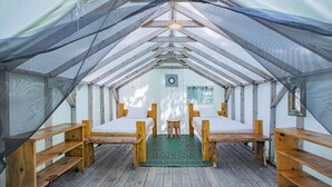 Una carpa con dos camas, bancos de madera y una alfombra verde.