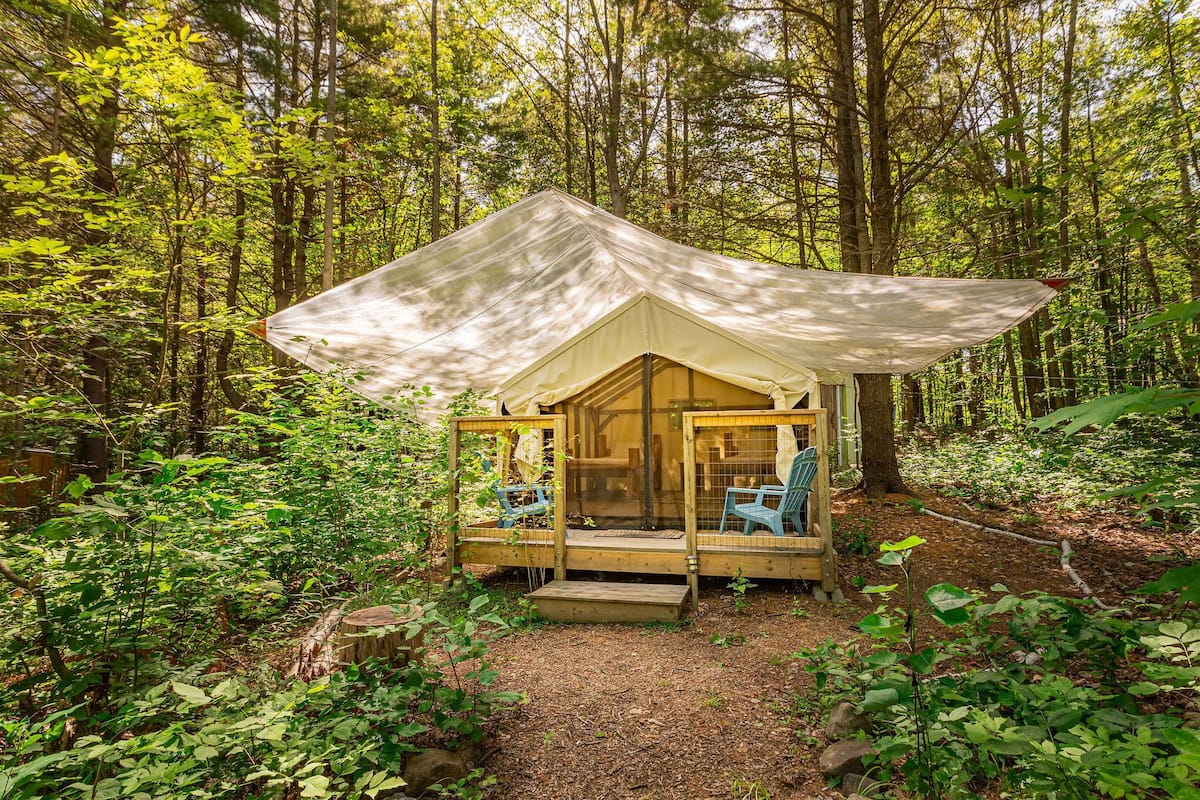 A forested campsite with a tent, two chairs, and a wooden deck.