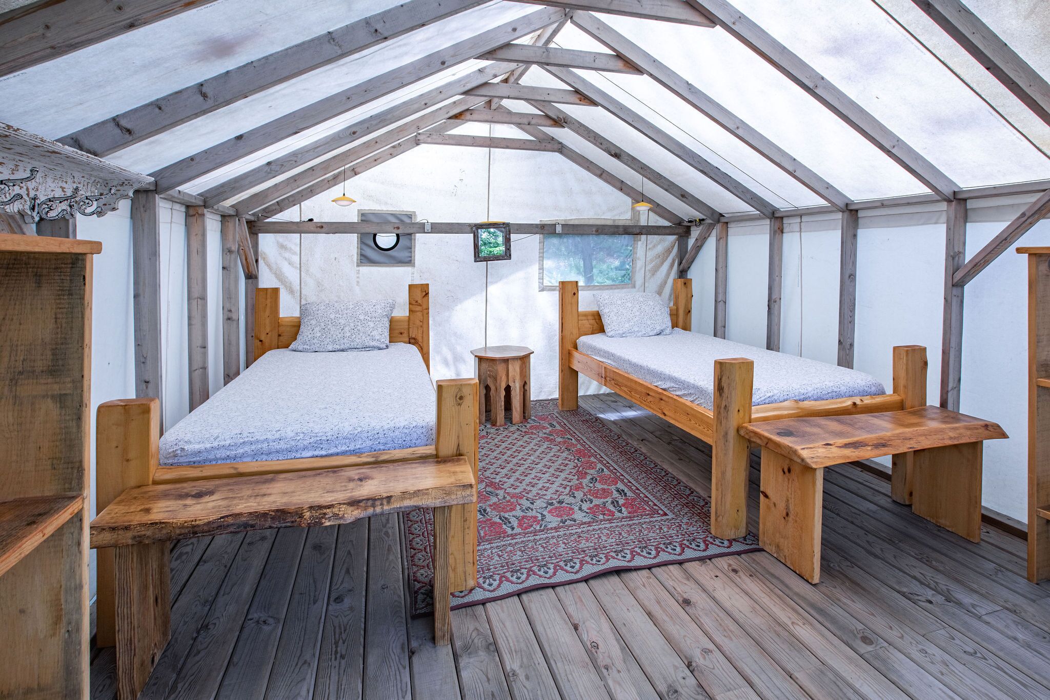 A tented room with two wooden beds, a small table, and a red patterned rug.