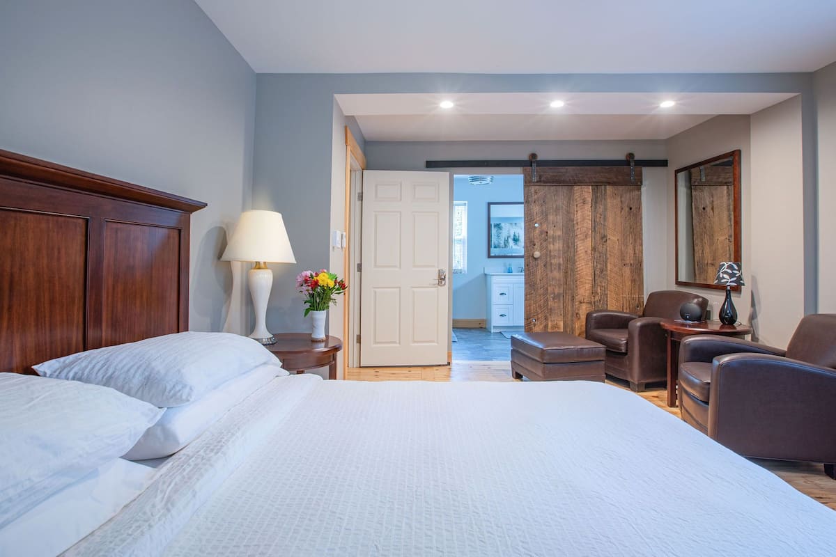 A hotel room with a large bed, a desk with a chair, a wooden wardrobe, and a bathroom visible through an open door.
