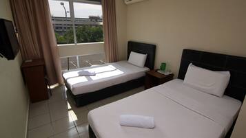 Una habitación de hotel con dos camas, una ventana con cortinas, una mesita con una taza verde y un equipo de aire acondicionado en la pared.