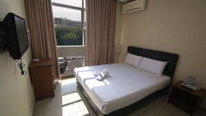 Habitación de hotel con una cama, televisión, una mesita y una ventana con cortinas.