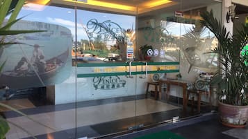 Entrada de hotel con puerta de vidrio, felpudo y vista de un barco en el agua a través del cristal.