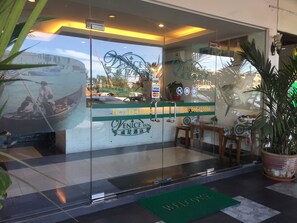 A hotel entrance with a glass door, a welcome mat, and a view of a boat on the water through the glass.