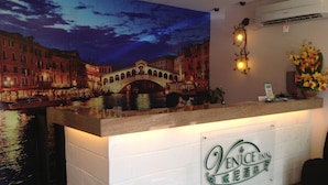 Una recepción con el letrero del Hotel Venetian Inn, un mural de un puente y un arreglo floral.