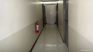 Un pasillo con un extintor fijado a la pared, puertas a ambos lados y una lámpara en el techo.