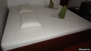 Una cama bien hecha con sábanas blancas y dos almohadas decorativas verdes.