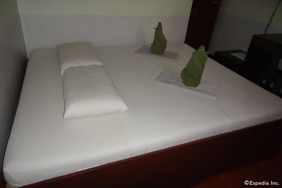 A neatly made bed with white linens and two decorative green pillows.