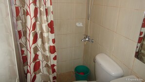Un baño con ducha, inodoro y un balde.