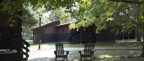 Una cabaña con dos sillas Adirondack bajo un árbol, una terraza de madera y una escalera que lleva a la cabaña.