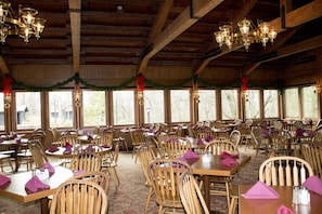 Un restaurante con mesas y sillas de madera, ventanas amplias y candelabros.
