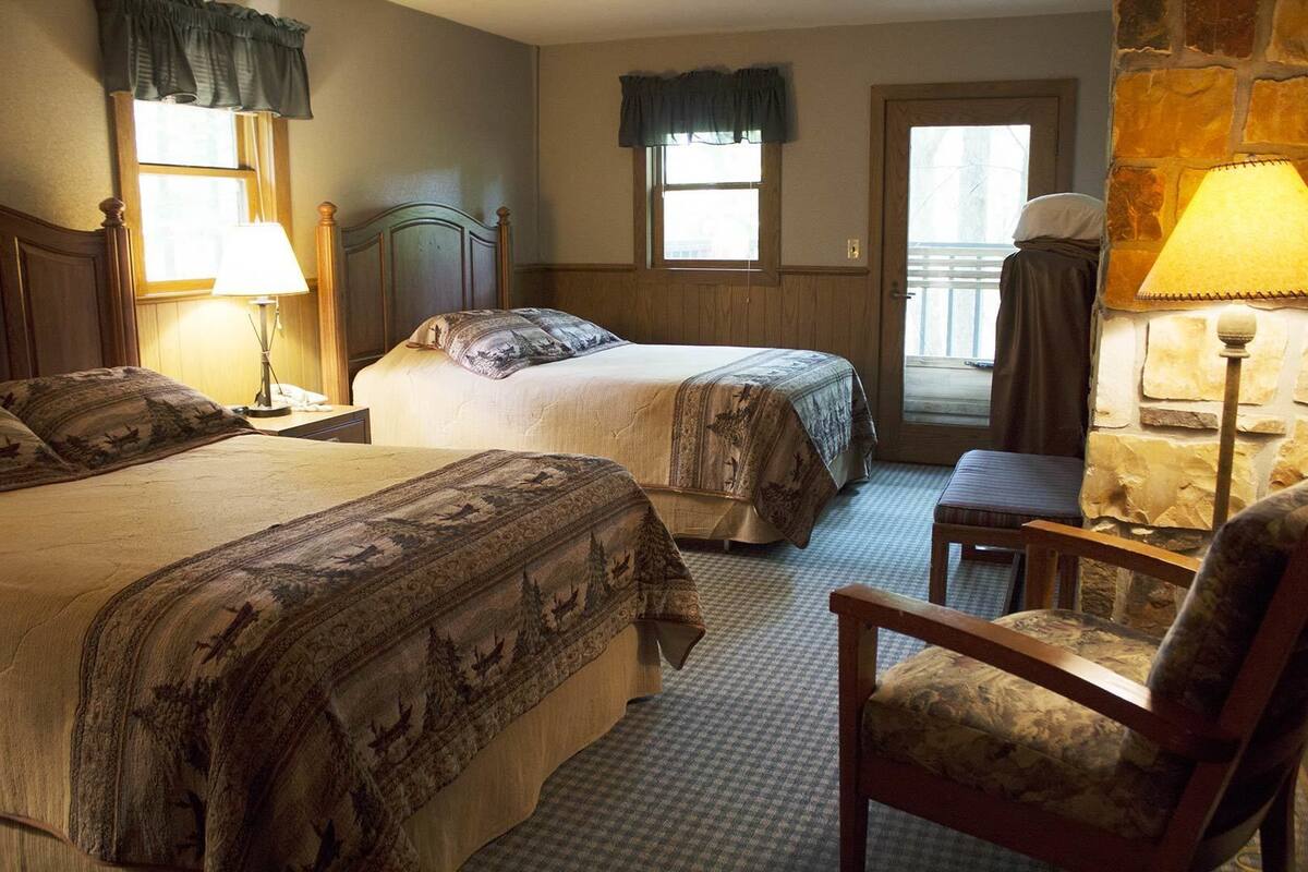 A hotel room with two beds, a chair, a lamp, and a window with curtains.