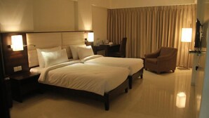 A hotel room with two beds, a desk, a chair, and a large window with curtains. - Beacon T2 Mumbai (Mumbai)