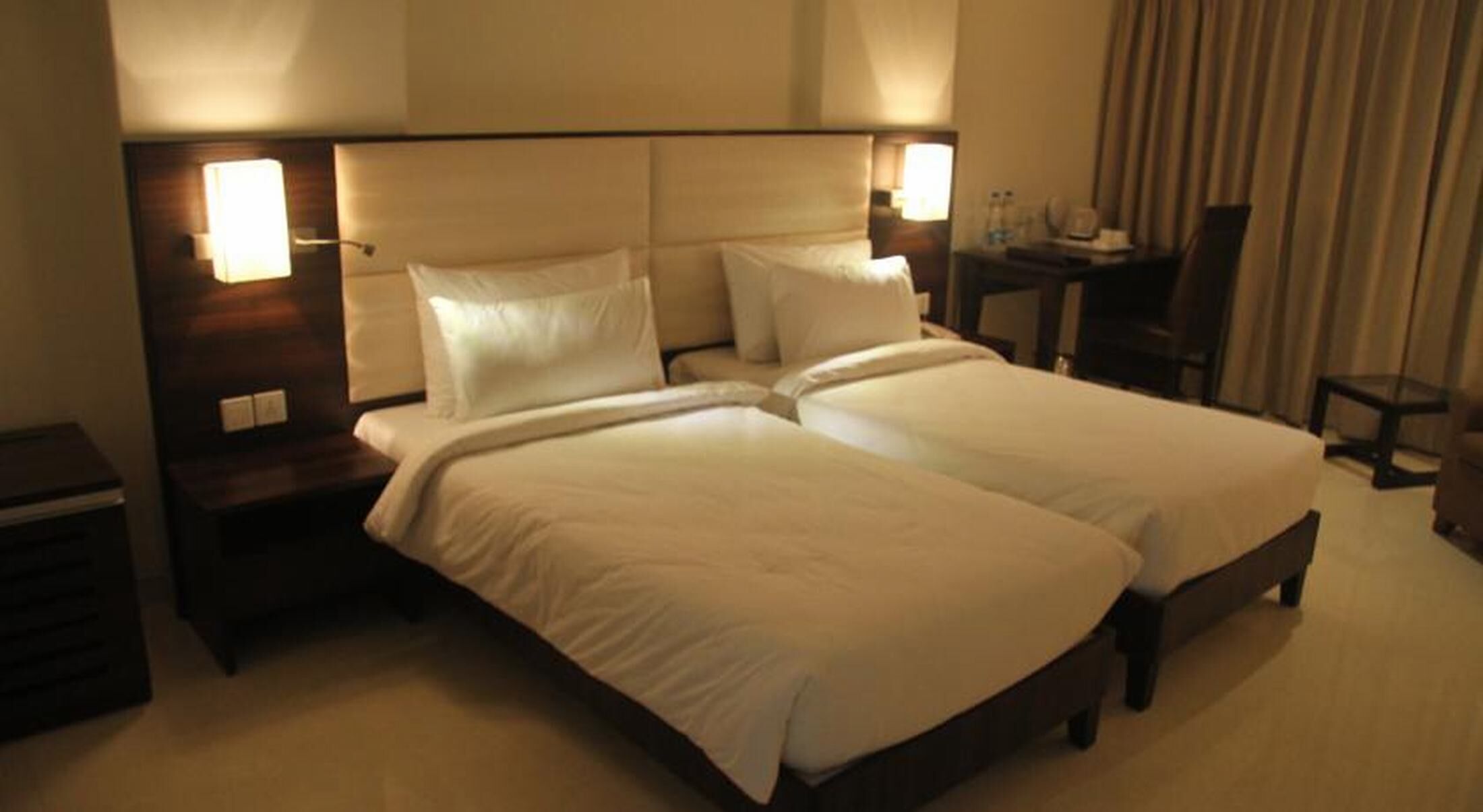 Un lit double avec deux oreillers, une table de chevet avec une lampe, une petite table avec une chaise et une fenêtre avec des rideaux.