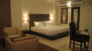 A hotel room with a bed, two bedside tables, a chair, a desk, and a mirror. - Beacon T2 Mumbai (Mumbai)