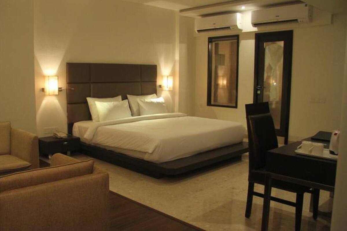 Una habitación de hotel con una cama, dos mesitas de noche, una silla, un escritorio y un espejo.