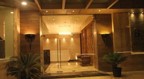 A reception area with a glass partition, wooden walls, and a chandelier. - Beacon T2 Mumbai (Mumbai)
