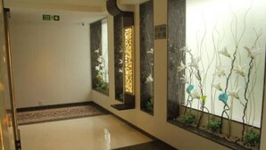 A hallway with a marble floor, a decorative wall with a floral pattern, and a green exit sign. - Beacon T2 Mumbai (Mumbai)