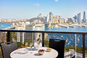 A balcony with a table, a bottle of champagne, a glass, a bowl of strawberries, and a view of the Sydney Opera House and Sydney Harbour. - Meriton Suites North Sydney (North Sydney)