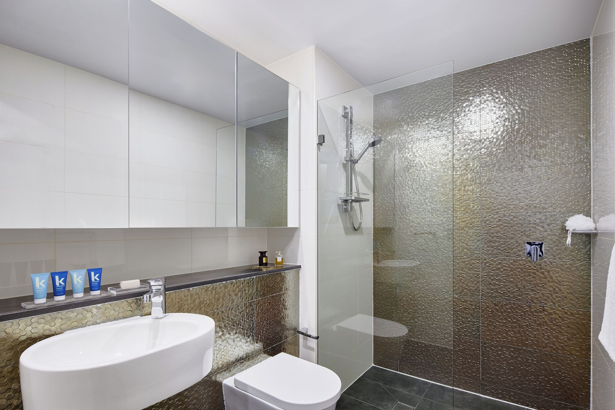A modern bathroom with a glass-enclosed shower, a white sink, and a toilet.
