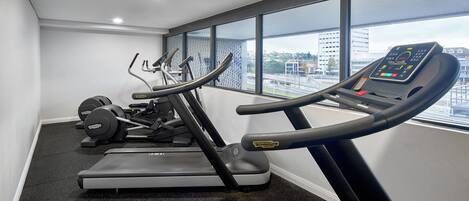 A gym with treadmills, ellipticals, and weight machines, large windows with a city view.