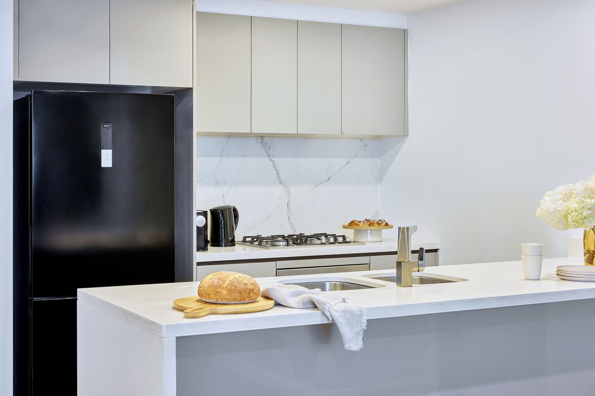 Een moderne keuken met een zwarte koelkast, een gasfornuis en een marmeren achterwand.