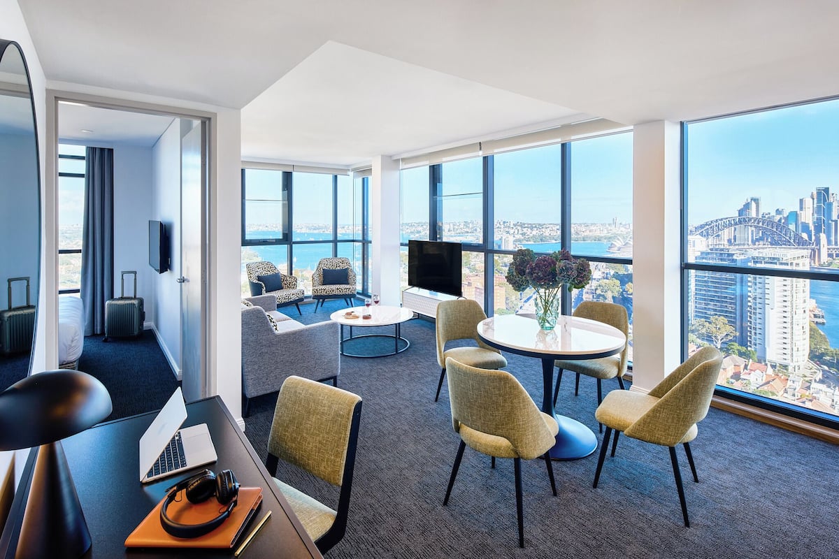 A modern hotel room with a large window, a laptop, a desk, and a seating area with a view of the city.