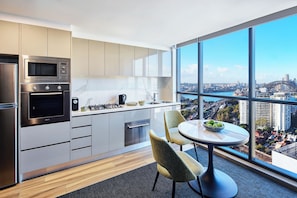 A modern kitchen with stainless steel appliances, a dining area with a round table and chairs, and a large window offering a city view.