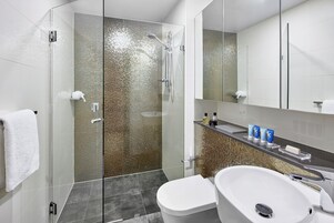 Un baño moderno con ducha acristalada, lavamanos blanco y un espejo grande sobre el mueble.