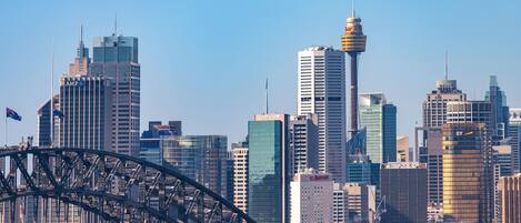 A city skyline with modern high-rise buildings, a prominent tower, and a bridge in the foreground.