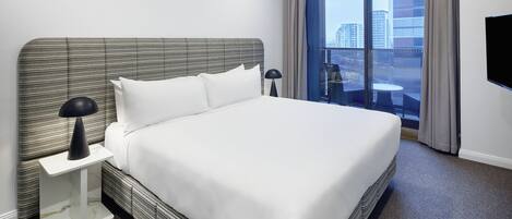 A hotel room with a large bed, a nightstand, a lamp, a TV, and a balcony with a city view.