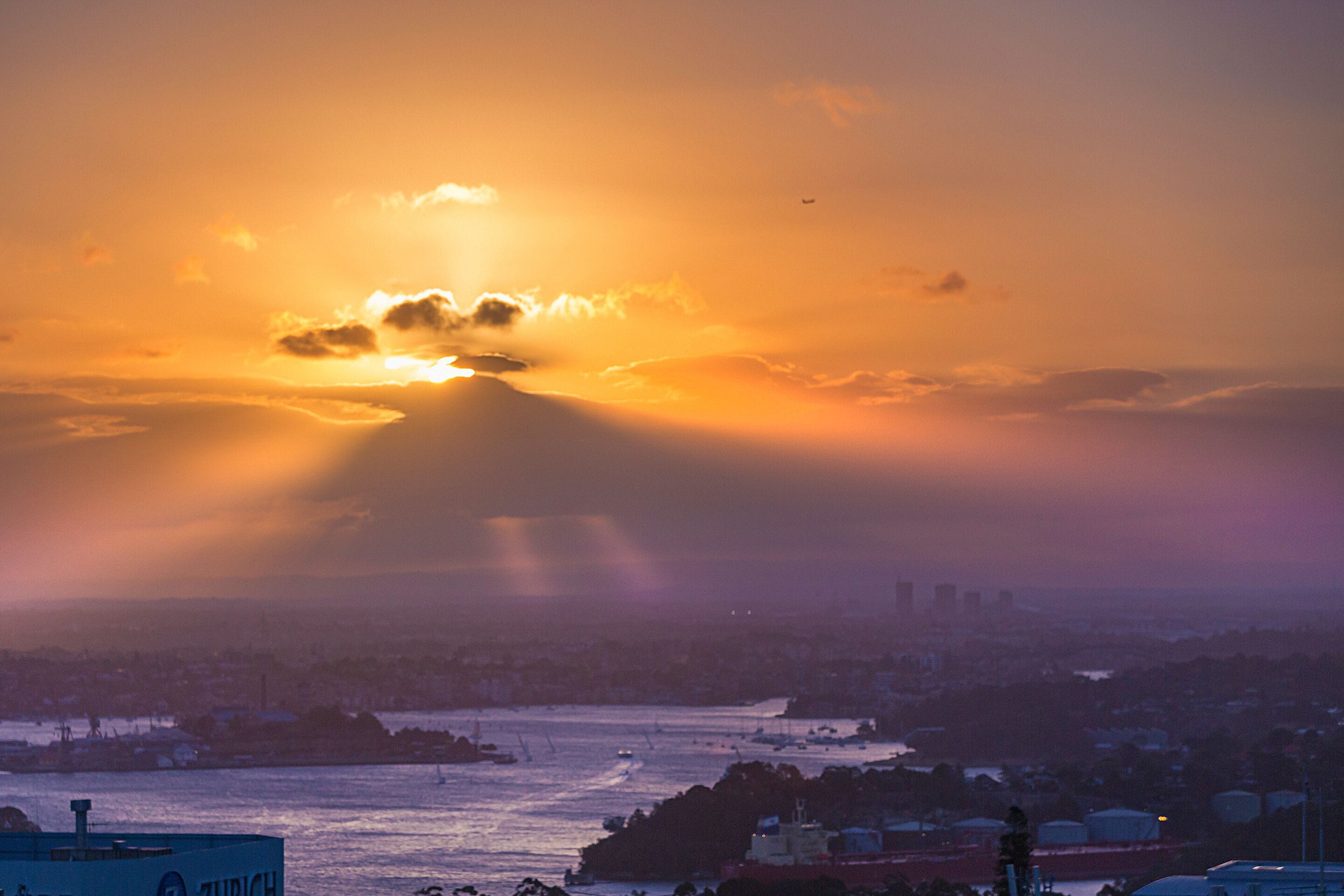 Un paisaje urbano al atardecer con un barco visible y edificios industriales.