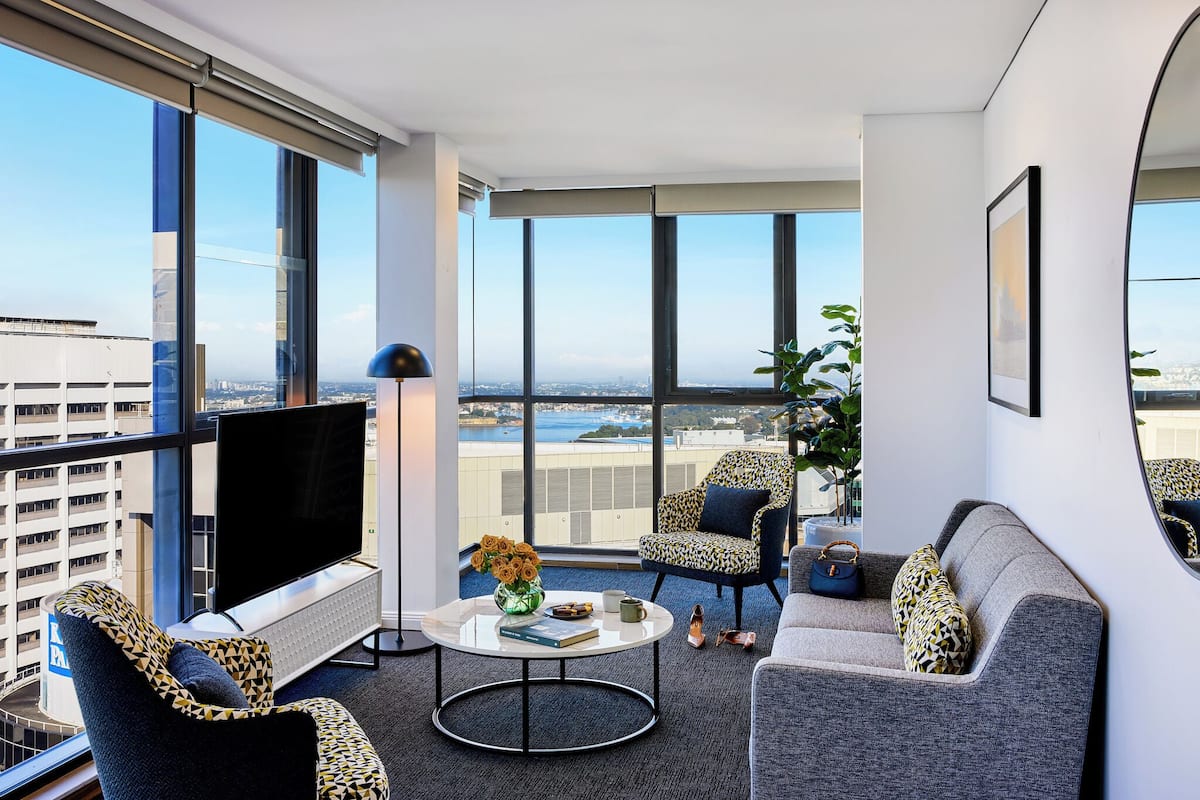 A modern living room with a large TV, comfortable seating, a coffee table, and a view of the city.