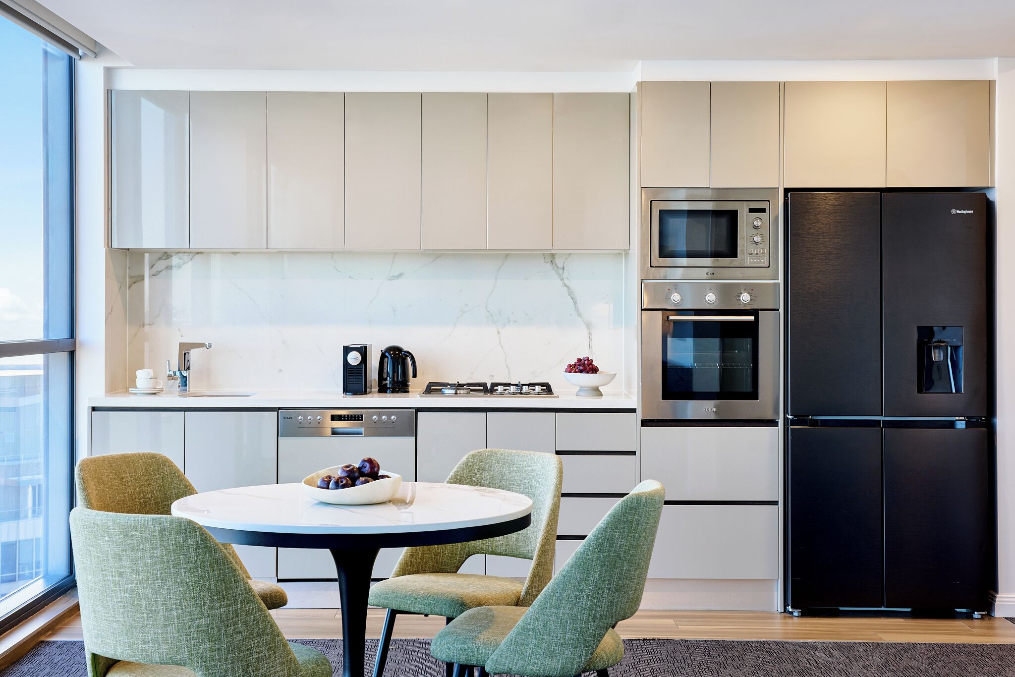 A modern kitchen with a dining area, featuring a round table, chairs, and a black refrigerator.