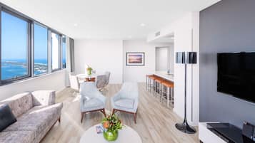 A modern living room with a large window, a sofa, two armchairs, a coffee table with a vase, a flat-screen TV, and a bar area.