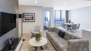 Een moderne woonkamer met een flatscreen televisie, een bank, een bijzettafeltje met een vaas, en een eethoek met een tafel en stoelen.
