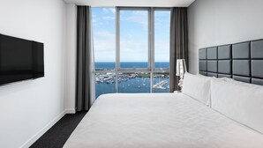 Hotelkamer met een groot bed, een flatscreen televisie aan de muur en uitzicht op de jachthaven door grote ramen.