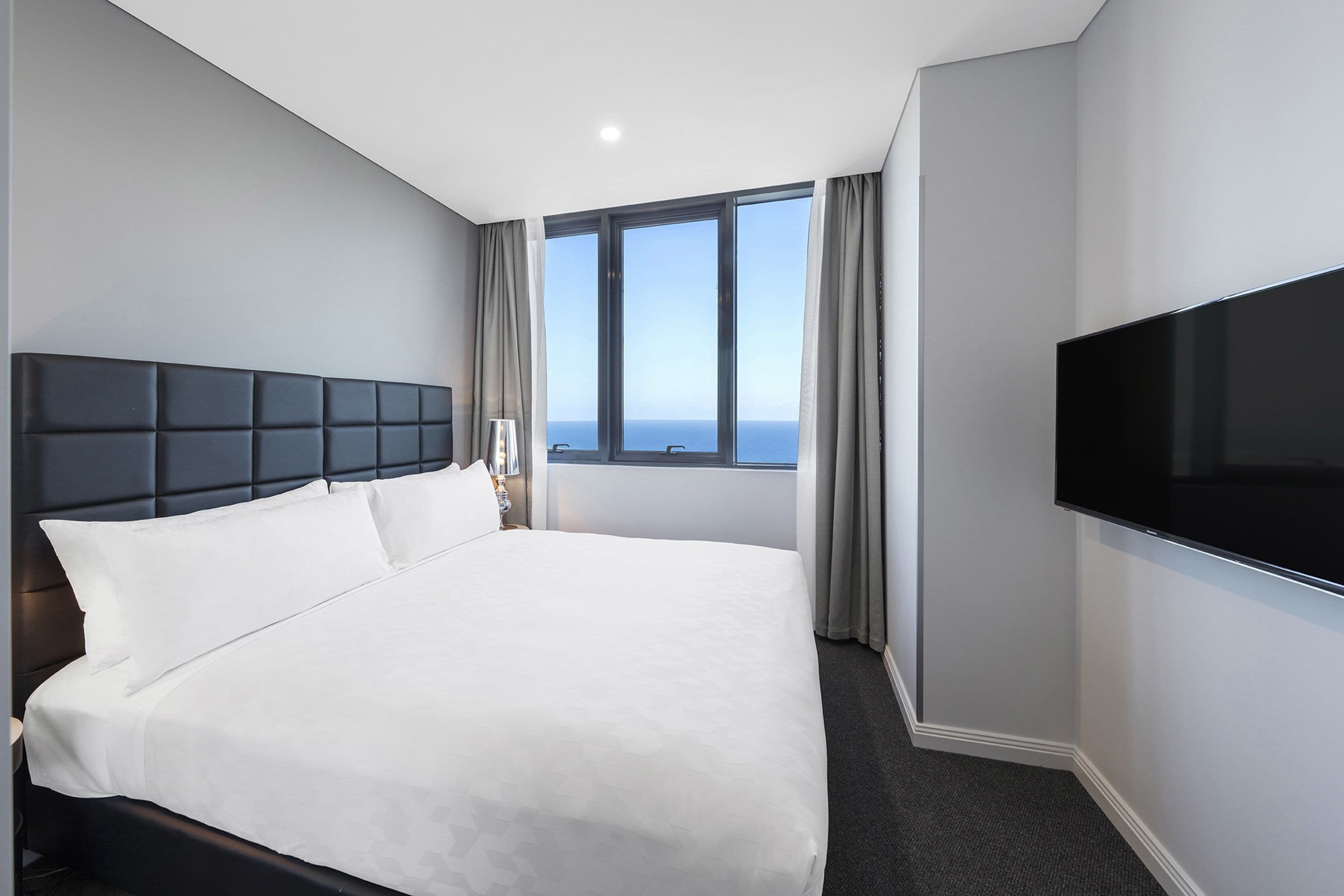 Une chambre d’hôtel dotée d’un grand lit, d’un téléviseur à écran plat et offrant une vue sur l’océan grâce à une grande fenêtre.