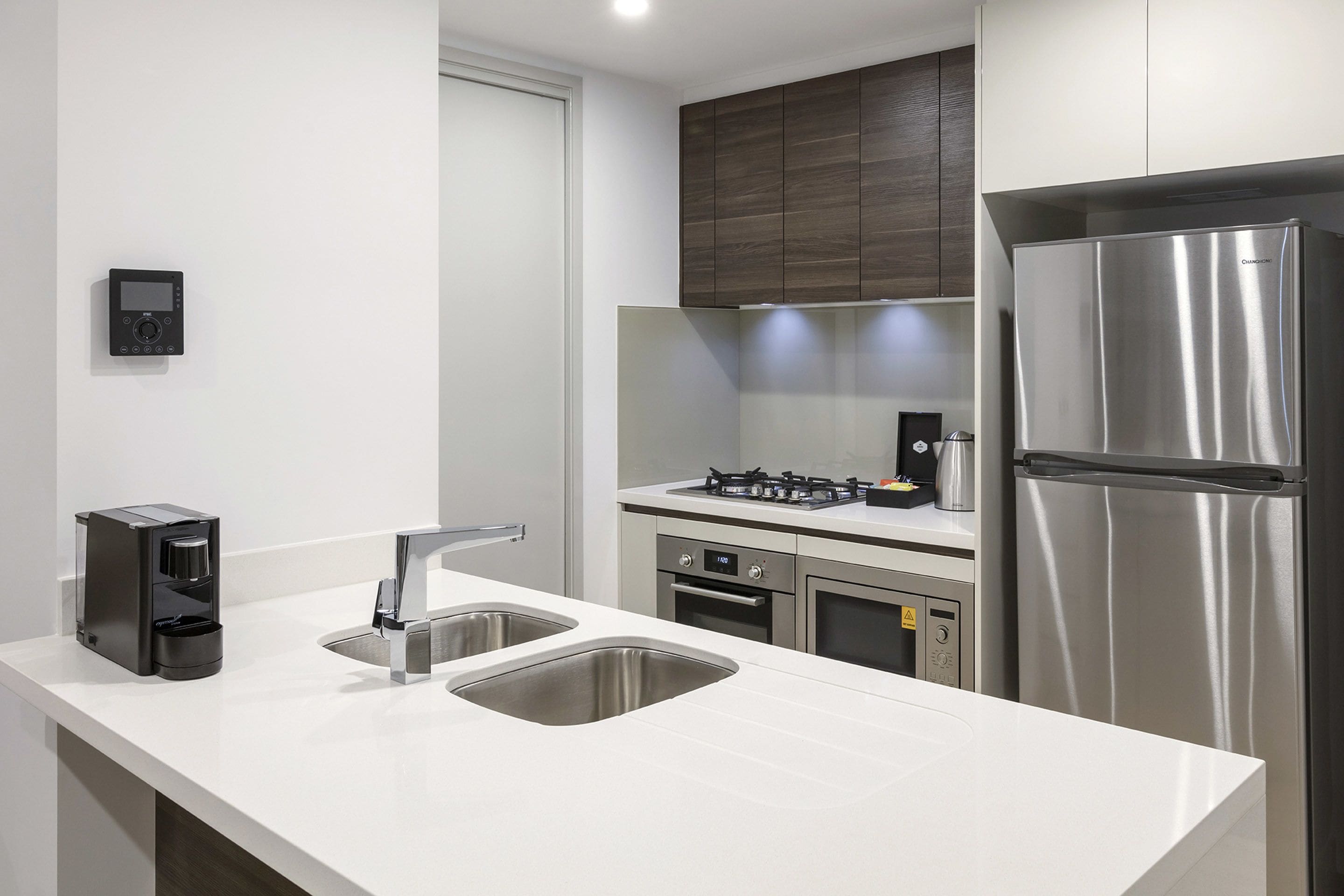 A modern kitchen with a stainless steel refrigerator, a coffee maker, and a double sink.