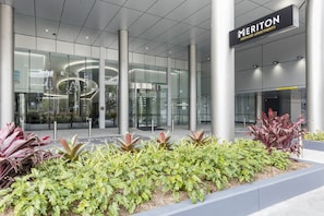 Entrada moderna de un hotel con fachada de vidrio, puerta giratoria y cartel de apartamentos con servicios Meriton.
